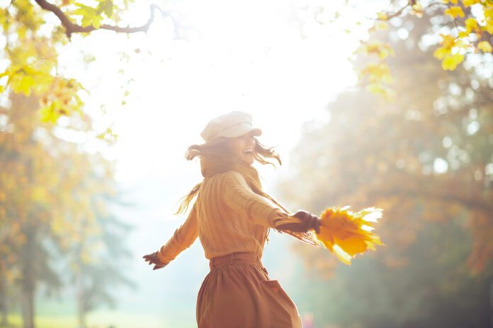 Woman with yellow leaves having fun time outside in autumn