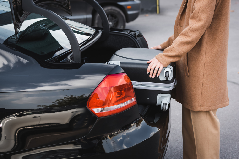 woman in autumn clothes putting suitcase in car trunk