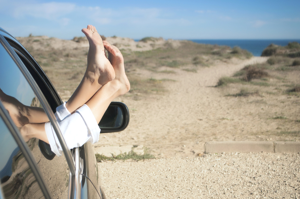 woman parked near beach with feet out of car window